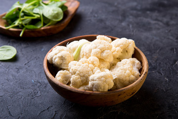 Fresh organic cauliflower cut into small pieces in wooden  bowl on stone background
