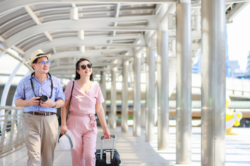 Fototapeta premium Elderly tourists, men and women, are walking dragging luggage. There is a building in the background during the daytime. Vacation travel concept