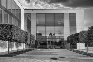 Greyscale shot of a modern building with glass windows and trees on the front