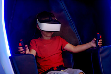 European boy wearing virtual reality helmet sitting in armchair and playing game. - 296826327