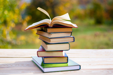 An open book lying on a stack of books in on a wooden table against the background of the garden.