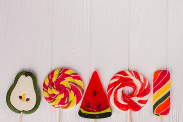 Border from large assorted lollipops. Row of fruit shaped candies on white wooden background with copy space.