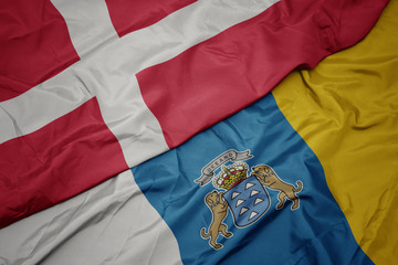 waving colorful flag of canary islands and national flag of denmark.