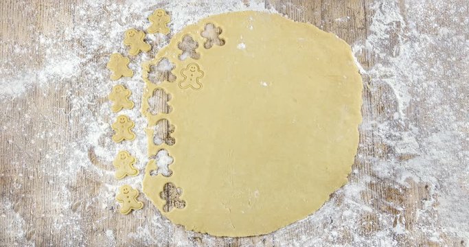 Stop motion in 4K of top view of raw dough that is being cut to make cookies shaped like funny gingerbread dolls on a floured wooden table. View from above. Recipes for children. Christmas desserts.