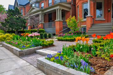 Fototapeta na wymiar This beautiful, urban front yard garden features a large veranda, brick paver walkway, retaining wall with plantings of bulbs, shrubs and perennials for colour, texture and winter interest.
