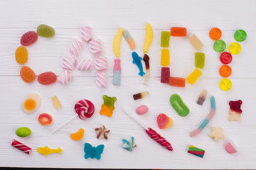 Flat lay composition from delicious colorful candies. CANDY word made from various candies on white wooden background.