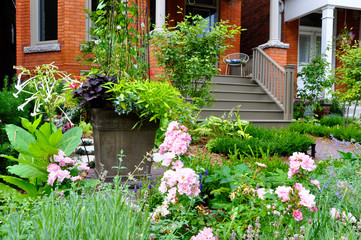 Fototapeta na wymiar This beautiful urban front yard garden features a large veranda, brick paver walkway, retaining wall with plantings of bulbs, shrubs and perennials for colour, texture and winter interest.