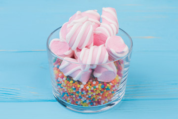 Glass jar with colorful sweets on blue background. Glassware with marshmallows and sprinkles against color background.