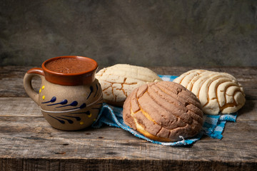 Mexican hot chocolate with sweet conchas bread on wooden background
