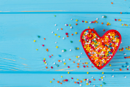 Valentines Day composition on blue background. Heart-shaped cookie cutter with candy sprinkles, copy space.