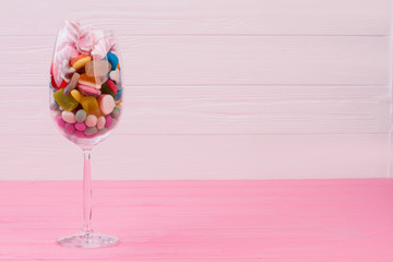 Wine glass filled with colorful candies. Multicolored candies and sweets in wine glass with copy space. Pastel wooden background.