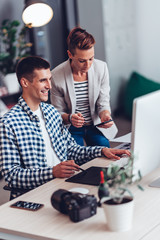 Graphic designer working on computer and talking with colleague