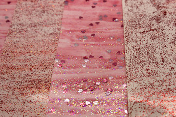 This is a photograph of an abstract background created by organizing stripes created using pink glitter paint and heart sequins