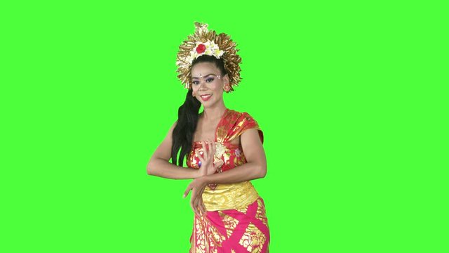 Attractive balinese dancer smiling at the camera while dancing in the studio. Shot in 4k resolution with green screen background