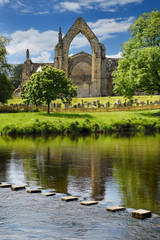 12th century Augustinian Bolton Priory church ruins with cemetery and stepping stones in River Wharfe at Bolton Abbey England