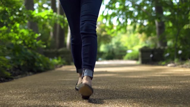 Low angle shot of Young woman walking outside in city park during the day. Focused only on the feet and shoes with shallow depth of field
