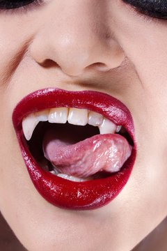 Sexy vampire. Women's lips with red lipstick. Tongue licking vampire fangs,