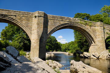 Fototapeta na wymiar 14th Century Devil's Bridge over the River Lune in Kirkby Lonsdale with sunbathers under blue sky Cumbria England