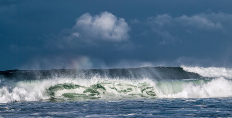 Seascape. Powerful ocean wave on the surface of the ocean. Wave breaks on a shallow bank. Stormy weather, stormy clouds sky background.