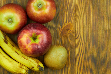 Close up view of red apples, bananas and kiwi on wooden background with copy space for text