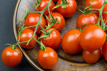 Bunch of fresh red cherry tomatoes with water drops in a plate on a dark background.