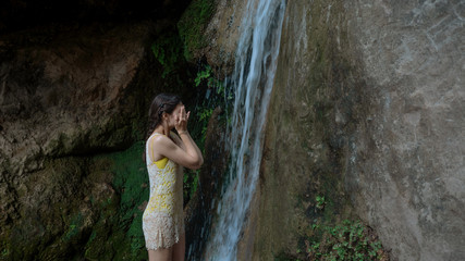 girl washes her face under the waterfall in the woods. Young woman in swimsuit in mountain river