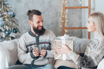 Christmas home celebration. Lady holding gift box for her boyfriend. Cozy festive interior background.