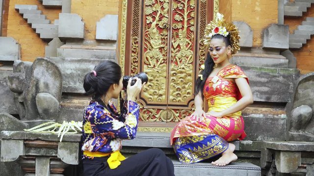 Female photographer taking picture of pretty balinese dancer in a temple. Shot in 4k resolution