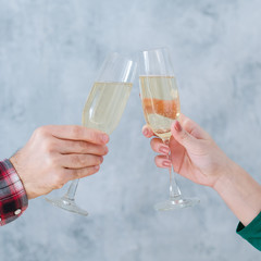 Holiday celebration. Cropped shot of couple clinking champagne glasses over blur gray wall background. Copy space.