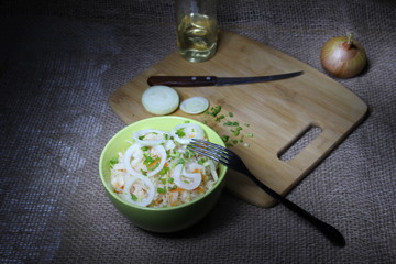 bowl of pickled cabbage with green and white onion and oil on wooden cutting board  with fork,...
