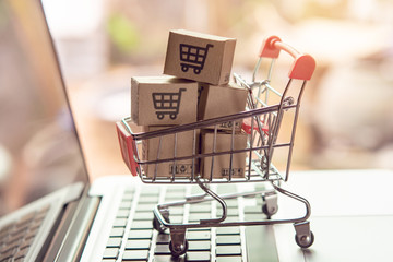 Shopping online. Parcel or cardboard boxes with a shopping cart logo in a trolley on a laptop...