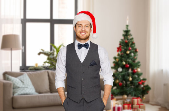 celebration, people and holidays concept - happy man in santa hat and suit over christmas tree on home background