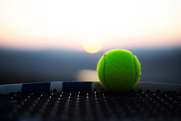 Close-up of tennis ball on net of racket at sunset.