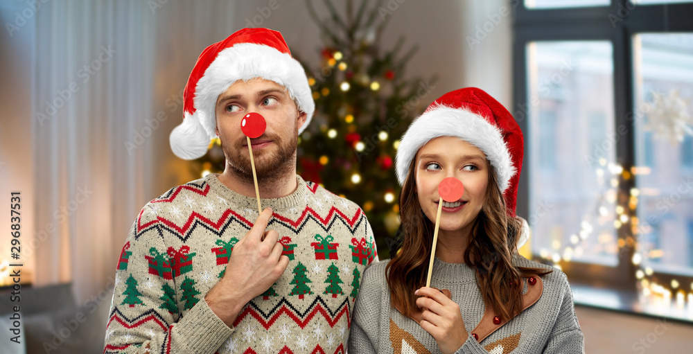 Wall mural celebration and holidays concept - happy couple in ugly sweaters posing with party props over christmas tree lights and home background