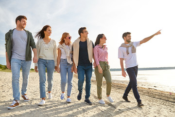 Obraz premium friendship, leisure and people concept - group of happy friends walking along beach in summer