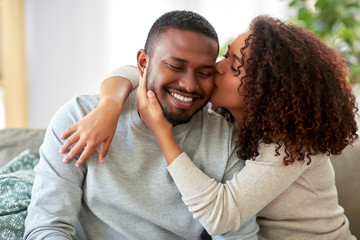 love, valentines day and relationships concept - happy african american couple sitting on sofa at...