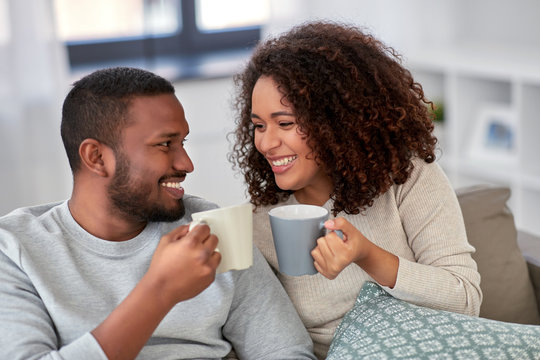 leisure and people concept - happy african american couple drinking coffee or tea at home