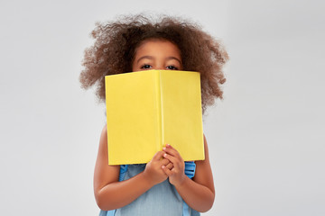 childhood, school and education concept - happy little african american girl with book over grey background