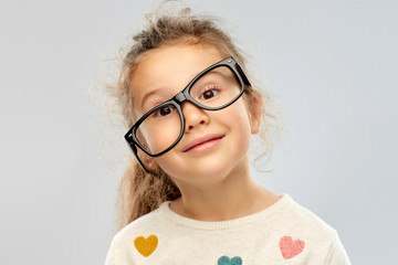 school, education and vision concept - portrait of smiling little girl in crookedly placed glasses...