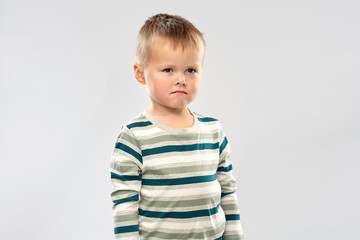 childhood and people concept - portrait of sad little boy in striped shirt over grey background