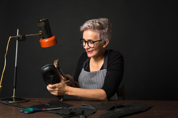 stylish woman in glasses with glasses on black background repairs shoe
