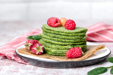Stack of thin green spinach pancakes, for healthy eating, diet, on plate with raspberries, red striped napkin, light photo, minimalism, horizontal