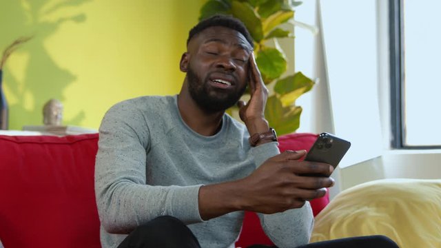 Upset african man receiving bad news on smartphone going crazy of internet deceive covering face in sadness and embarassment.