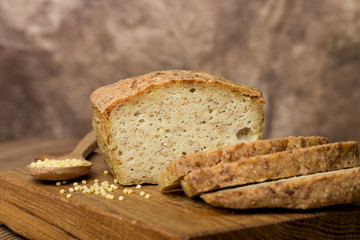 bakery products, freshly baked golden bread, cut pieces, millet, flax, grain scattering, wooden board, spoon, brown background, horizontal