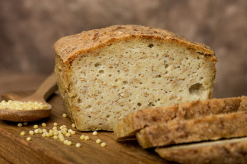 bakery products, freshly baked golden bread, cut pieces, millet, flax, grain scattering, wooden board, spoon, brown background, horizontal