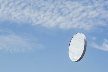 Round mirror in blue sky reflecting clouds