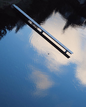 Wooden pier on lake reflecting blue sky