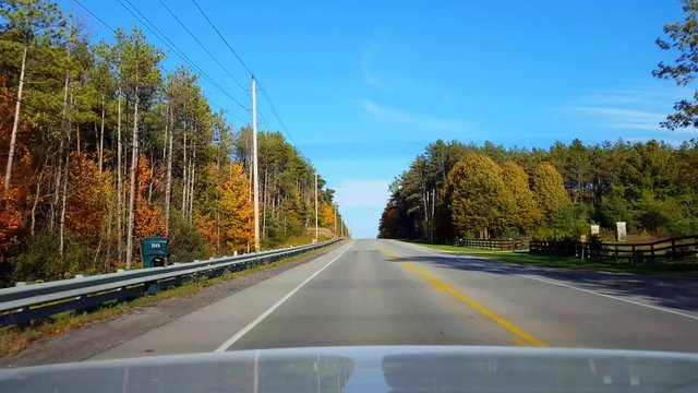 Rear View From Back of Car Driving Rural Countryside Road During Autumn Day.  Car Point of View POV Behind Vehicle Country Street in Fall Season With Colored Leaves.