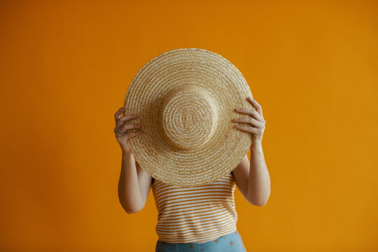 Woman holds up a straw hat in front of face