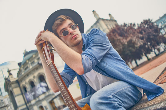 Young man playing the guitar. Stylish hipster guy with hat enjoys music and holidays.